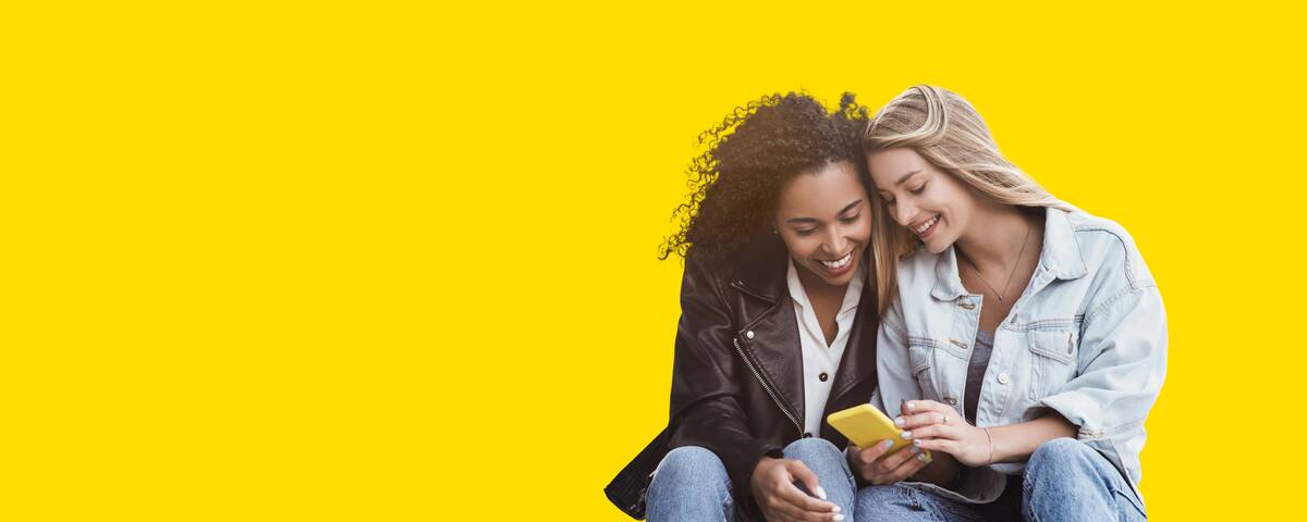 Zwei Frauen sitzen lächelnd nebeneinander und schauen auf ihr Handy