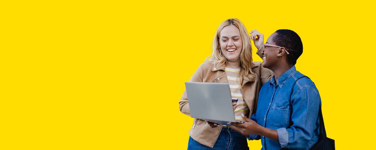 Zwei Frauen lächeln während sie auf den Laptop schauen.