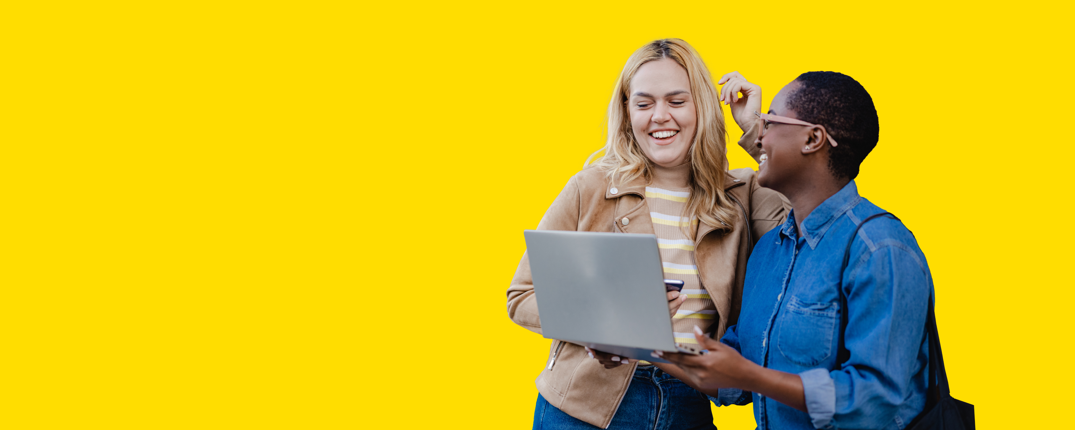 Zwei Frauen lächeln während sie auf den Laptop schauen.